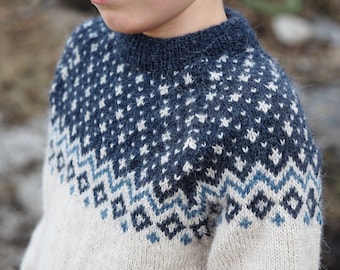 May include: A white and blue knitted jumper with a traditional Scandinavian pattern. The jumper has a crew neck and long sleeves.