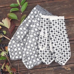 May include: A pair of gray and white knitted mittens with a geometric pattern. The mittens are folded and laid out on a wooden surface.