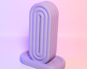 May include: A lavender-colored, abstract sculpture with a rounded rectangular form. The sculpture has a series of parallel, curved lines that create a textured surface. It sits on a matching oval base, all against a gradient background.