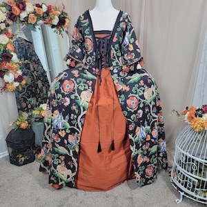Puede incluir: Un vestido de estilo histórico sobre un maniquí. El vestido presenta una chaqueta negra con estampado floral sobre una falda color óxido. La chaqueta tiene un escote cuadrado y se ata con cordones en la parte delantera. Las mangas tienen adornos decorativos. El texto "Being Sew Weird" es visible.