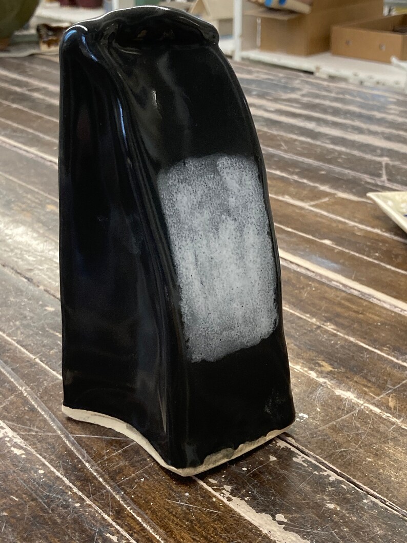 May include: Black ceramic vase with a white glaze on one side. The vase has a unique, asymmetrical shape.
