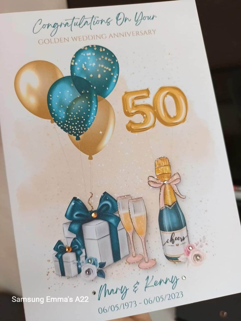 May include: A golden 50th anniversary card with teal and gold balloons, a bottle of champagne, two champagne glasses, and two gift boxes. The card says "Congratulations on your Golden Wedding Anniversary" and "Mary & Kenny 06/05/1973 - 06/05/2023".