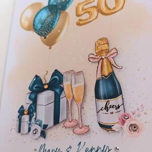 May include: A gold 50th anniversary card with a champagne bottle, two champagne flutes, and two gift boxes with teal and white ribbons. The card has a pink and white floral design with gold glitter. The text on the card reads "Mary & Kenny" and "06/05/1973 - 06/05/2023".