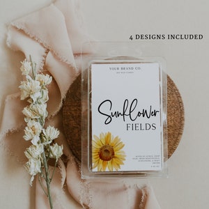 May include: A soy wax candle with a white label that says "Your Brand Co." and "Sunflower Fields". The label also includes a blend of citrus, crisp pear, fresh honeysuckle, sunflowers, and dewy orchid scents. The candle is packaged in a clear plastic container and is sitting on a wooden surface.