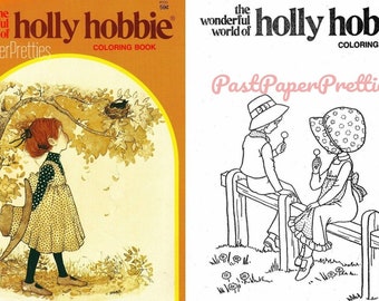 May include: A coloring book cover featuring a black and white illustration of two children sitting on a fence, holding lollipops. The title of the book is "The Wonderful World of Holly Hobbie Coloring Book" with the text "Past Paper Pretties" in pink.