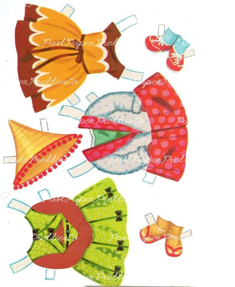 May include: A vintage paper doll set with various outfits and accessories. The set includes a yellow dress with brown trim, a red and white polka dot dress, a green dress with brown trim, a straw hat with red pom-poms, and two pairs of red shoes.