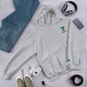 May include: A gray hooded sweatshirt with a green embroidered heart and the text "T-MAMA" on the front. The sweatshirt has a green shamrock embroidered on the left sleeve.