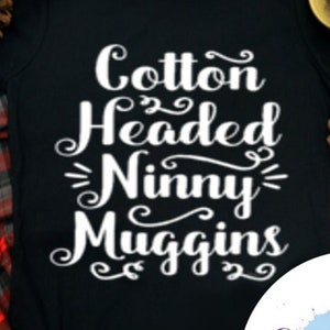 May include: Black t-shirt with white text that reads "Cotton Headed Ninny Muggins". The shirt is on a red and black plaid surface. A white circle with the text "Cool Tees & Freshies" is in the lower right corner.