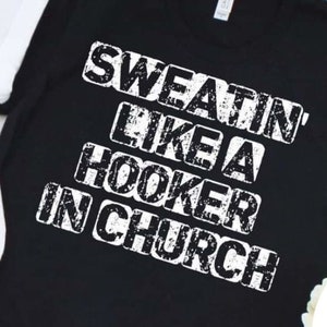 May include: Black t-shirt with white text that reads "Sweat'n Like A Hooker In Church".