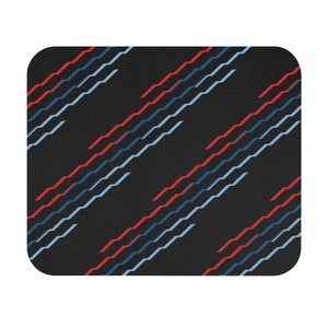 May include: A rectangular mousepad with rounded corners. The mousepad has a black background with diagonal lines in red and light blue. The lines have a zig-zag pattern.