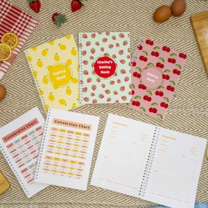 May include: Several spiral-bound baking books with fruit patterns: lemons, strawberries, and cherries. One book reads "Charley's Baking Book." Conversion charts and blank recipe pages are also visible.