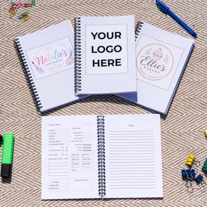 May include: A collection of white spiral-bound notebooks, ideal for business or personal use. The covers feature custom logos, including "Natalie's Artwork", "Your Logo Here", and "Ellie's Bakery". Interior pages are designed for notes and event planning.
