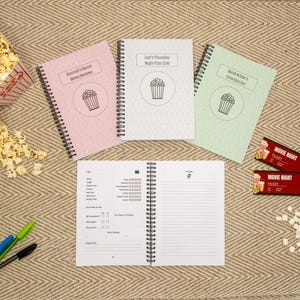 Könnte beinhalten: Spiralgebundene Notizbücher mit Popcorn-Grafiken und Texten: "Hannah's Horror Movie Reviews", "Dad's Thursday Night Film Club" und "Sarah & Jake's Directors Cut". Enthält Kinokarten und Popcorn.