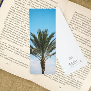 May include: Bookmark featuring a vibrant image of a palm tree against a bright blue sky. The bookmark has a rectangular shape and is printed on cardstock. The text "Javea Spain" and "ACOM STUDIO PRINTED IN ENGLAND" are visible.