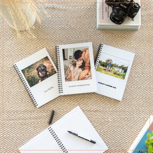 May include: Three spiral bound notebooks with different covers. The first notebook has a photo of a dog on the cover and the text "Laura's Wild Rides". The second notebook has a photo of a couple on the cover and the text "Lucy & Ben's Wedding Planning". The third notebook has a photo of a person gardening and the text "Grandad's Gardening Book".
