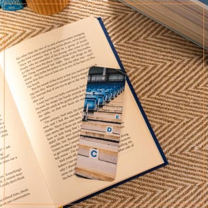 May include: A blue and white bookmark with a photo of stadium seating. The bookmark has the letters C, D, and E printed on the seats. The text on the bookmark reads "But the moral of the story is that you need to stop looking into this. Whoever's involved, they're dangerous. I'm worried that if you try to get in the way, they'll after you."