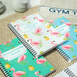 Può includere: Quaderni a spirale con motivi di fenicotteri e ananas. I quaderni hanno titoli come "Transformation Journal" e "Harriet's Transformation Journal". I quaderni sono in vari colori, tra cui bianco, verde acqua e azzurro.