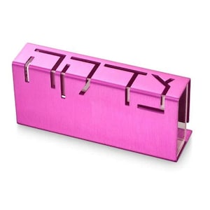 May include: A pink metal mezuzah case with the Hebrew word "Shabbat" cut out in the front.