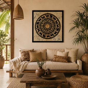 Op de afbeelding: Een vierkant wandkunstwerk met een zwart cirkelvormig mandala-ontwerp met dierensilhouetten op een crèmekleurige batikstoffen achtergrond, ingelijst in een dunne zwarte rand, geplaatst boven een beige bank met diverse gestructureerde kussens.