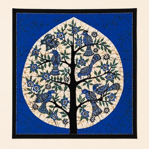 May include: A square textile wall hanging featuring a batik-style design of a black tree with blue birds and a butterfly perched on branches. The tree is set within a cream-colored oval against a deep blue background with a black border.