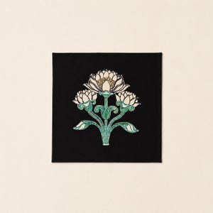 May include: A square black textile featuring a central graphic of three stylized lotus flowers. The flowers are white with gold centers, supported by green stems and leaves with intricate line work, creating a symmetrical botanical design.