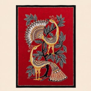 May include: A framed artwork featuring two stylized peacocks perched on a tree branch against a red background. The peacocks are primarily gold and brown with detailed feather patterns. The tree is black with green leaves, and the frame is black.
