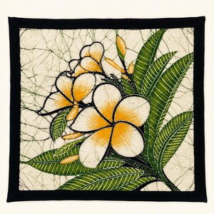 May include: A square textile wall hanging featuring a batik-style print of white and yellow plumeria flowers with green leaves. The background has a cream-coloured crackle pattern, and the entire piece is framed by a solid black fabric border.