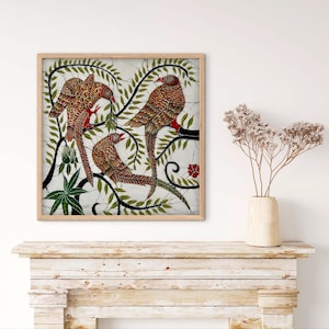 Puede incluir: Una obra de arte enmarcada con tres pájaros de plumaje rojo y marrón posados en una rama con hojas verdes. Los pájaros están sobre un fondo blanco con un diseño floral. La obra está en un marco de madera.