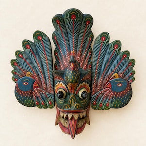 Puede incluir: Una máscara de madera tallada a mano con un rostro central de ojos grandes y saltones, dientes afilados y lengua saliente. La máscara está flanqueada por dos paneles laterales que representan aves estilizadas con abanicos de plumas.