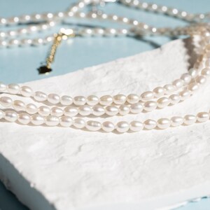 May include: A white pearl necklace with multiple strands of pearls. The necklace is on a white surface.