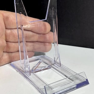 Puede incluir: Soporte de exhibición de plástico transparente con base rectangular y soporte en ángulo. Diseñado para sostener objetos en posición vertical, exhibiéndolos. Fabricado en plástico transparente.