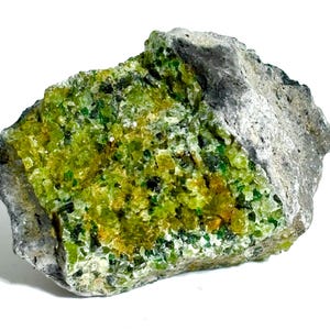 May include: A raw mineral specimen featuring a cluster of vibrant lime green and yellow crystalline structures embedded within a rough, grey, rocky matrix. The crystalline surface displays a granular texture with varying shades of green.