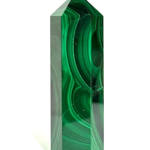 Può includere: Una torre in cristallo di malachite lucida con base esagonale e punta. La pietra presenta bande concentriche e motivi vorticosi di colore verde bosco intenso e verde smeraldo chiaro su tutta la superficie liscia, verticale e sfaccettata.
