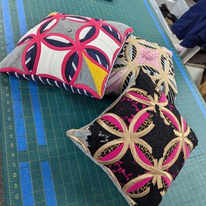 May include: Three square throw pillows featuring a geometric circular appliqu&eacute; pattern. The first pillow has grey, white, navy, and hot pink fabric. The second is beige and pink. The third features black lace, leopard print, and hot pink fabric.