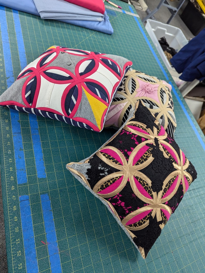 May include: Three square throw pillows featuring a geometric circular appliqu&eacute; pattern. The first pillow has grey, white, navy, and hot pink fabric. The second is beige and pink. The third features black lace, leopard print, and hot pink fabric.