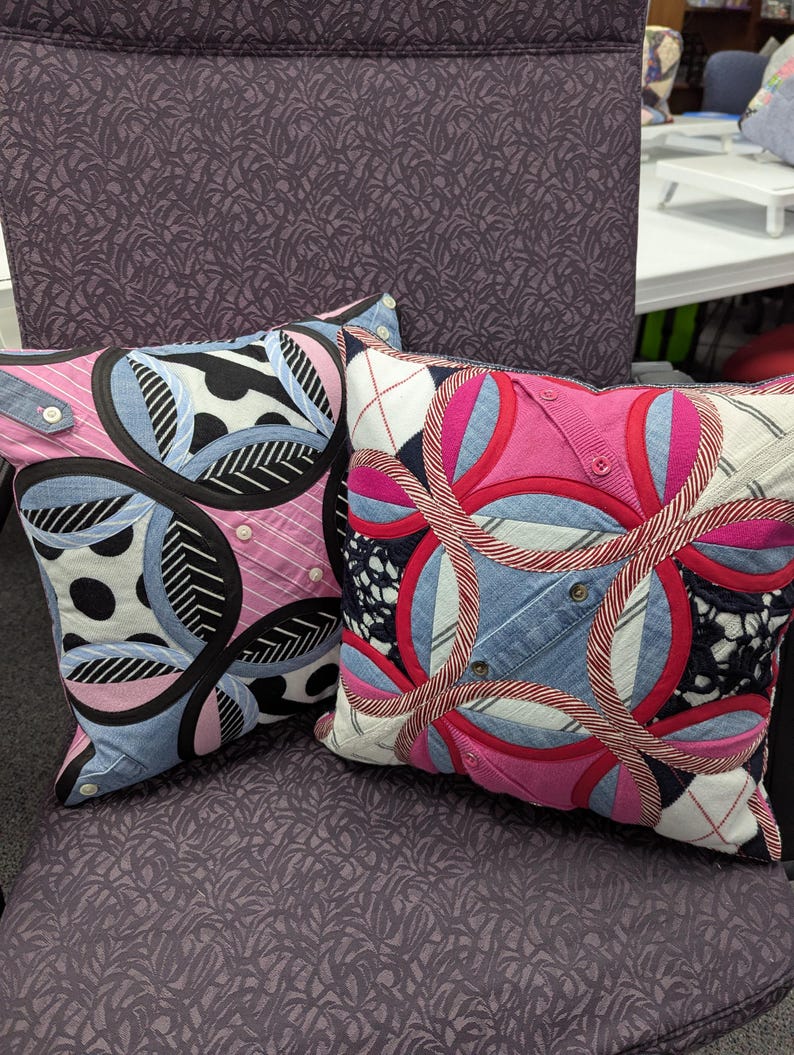 May include: Two square throw pillows featuring a patchwork design of mixed fabrics including denim, pink striped cotton, and black and white patterns. The pillows are constructed with circular motifs, visible buttons, and stitched seams throughout.