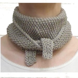 Könnte beinhalten: Ein taupefarbener Strick-Halswärmer mit texturiertem Kraus-Rechts-Strickmuster. Das Accessoire ist so konzipiert, dass es um den Hals gewickelt wird und eine kleine integrierte Schlaufe zum Befestigen eines Endes besitzt, was eine gefaltete Optik erzeugt.
