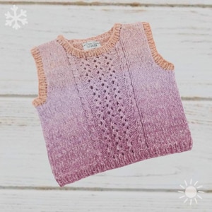 Könnte beinhalten: Eine gestrickte Weste in einem Farbverlauf aus Rosatönen, der von hellen zu dunklen Schattierungen übergeht. Das ärmellose Kleidungsstück hat ein strukturiertes Design mit einem zentralen Lochmuster und einem gerippten Halsausschnitt und Armausschnitten in Pfirsichfarbe. Das Etikett lautet "La Chou D'Or".