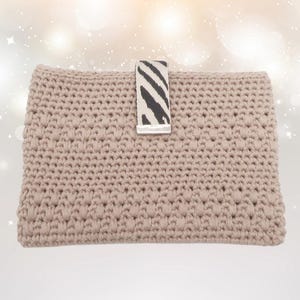 Könnte beinhalten: Beige gehäkelte Clutch mit strukturiertem Muster. Die Clutch hat einen Zebra-Print-Riemen mit einem silberfarbenen Metallverschluss. Die rechteckige Tasche scheint handgefertigt zu sein.