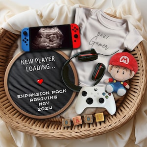 Puede incluir: Una cesta de mimbre llena de artículos para bebés, incluyendo un body blanco con el texto "BABY Gamer", una Nintendo Switch, un tablero de letras con el texto "NEW PLAYER LOADING... EXPANSION PACK ARRIVING MAY 2024", unos auriculares negros, un mando de videojuegos blanco y un personaje de peluche de Mario.