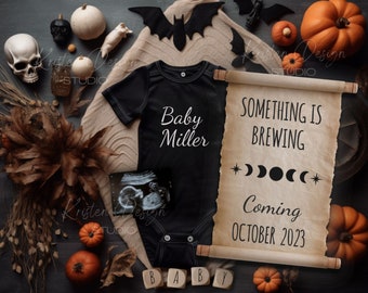 May include: A Halloween-themed baby announcement with a black onesie that says "Baby Miller" and a scroll that says "Something is brewing... Coming October 2023". The scroll is decorated with moons and stars. There are pumpkins, bats, and other Halloween decorations around the onesie and scroll.