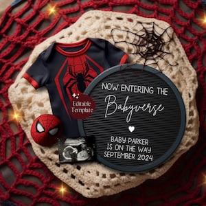 May include: A baby announcement featuring a Spider-Man themed onesie, a plush Spider-Man head, and a letter board. The letter board reads "Now Entering The Babyverse" with the baby's name and due date. The items are on a red and cream crocheted blanket.