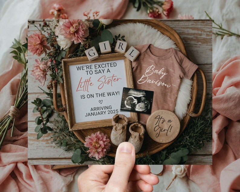 May include: A baby announcement card featuring a wooden tray filled with pink flowers, a pink onesie with the text "Baby Davison", a wooden sign that reads "We're excited to say a little sister is on the way! Arriving January 2025", a wooden sign that says "It's a girl!" and a small ultrasound image.