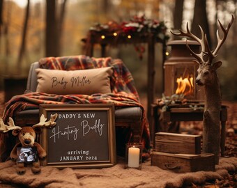 May include: A rustic scene with a framed sign that reads "DADDY'S NEW Hunting Buddy arriving JANUARY 2024." A plush deer toy holds a sonogram. A pillow with "Baby Miller" is on a plaid blanket. A deer statue and lantern with a fire complete the woodland theme.