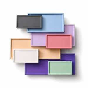 May include: A collection of rectangular trays in various colors, including gray, light blue, lavender, pink, peach, white, purple, and green. The trays are arranged in a layered, overlapping pattern against a white background.