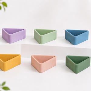 May include: Six colorful, triangular planters in shades of purple, green, blue, yellow, pink, and dark green. The planters are arranged on a white surface, showcasing their geometric design and vibrant colors. These planters are ideal for small plants or succulents.