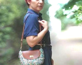 May include: A woman with short, bright red hair is wearing a dark blue shirt and a brown and iridescent crossbody bag. The bag has a brown leather flap with a gold clasp.