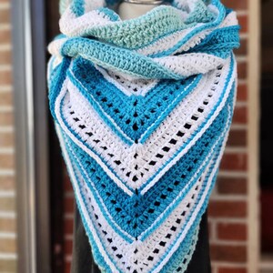 May include: A crocheted triangular shawl in shades of blue and white. The shawl is made with a lacy stitch pattern and has a fringed edge.