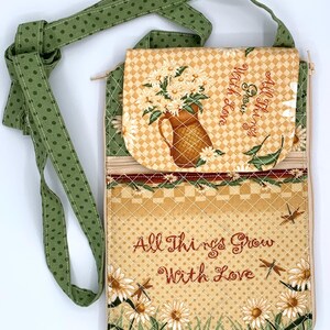 May include: Quilted crossbody bag with a green polka dot strap. The bag features a floral design with daisies and the embroidered text "All Things Grow With Love". The bag has a zippered pocket and a flap closure.