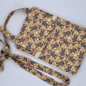 May include: A beige crossbody bag with a repeating pattern of sock monkey figures in gray, red, and white. The bag has a matching strap and a small flap closure. The bag is quilted with a diamond pattern and has a zipper closure.